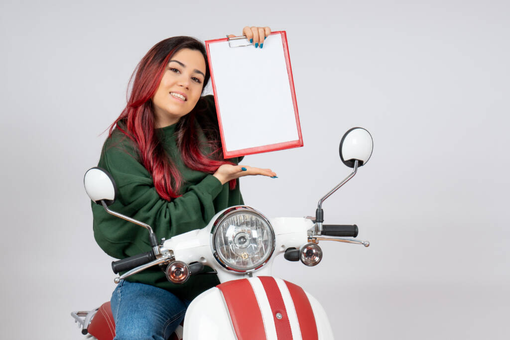poza din fata fata tanara pe motocicleta tinand in mana o semnatura